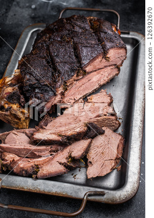 Roast Venison leg, baked meat of roe deer with bone on a tray with herbs. black background. top view 126392670