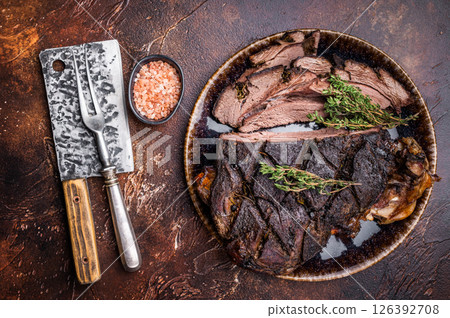 Baked and sliced Venison leg. roast meat of deer with bone on a plate. brown background. top view 126392708
