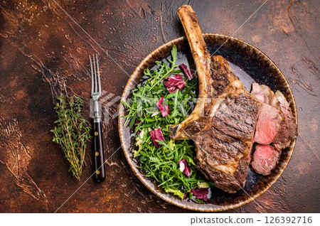 Grilled and sliced Tomahawk beef steak, marble rib eye with bone on plate with salad. brown background. top view Grilled and sliced Tomahawk beef steak, marble rib eye with bone on plate with salad. brown background. top view 126392716