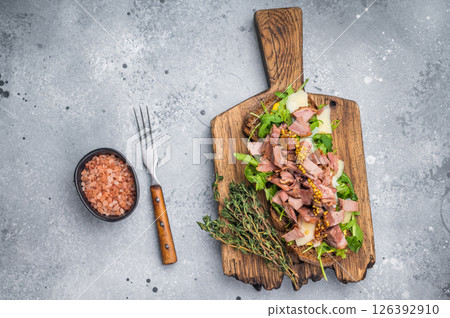 Open sandwich with duck fillet meat, foie gra liver, arugula and cheese on board. grey background. top view 126392910