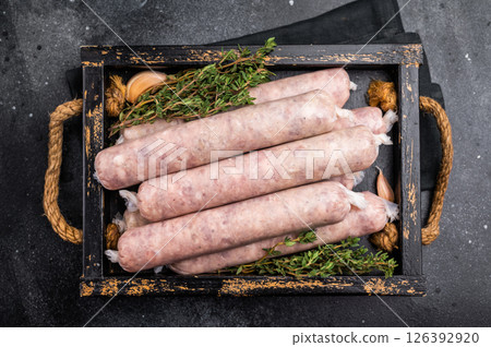 Raw Sausages with minced chicken and turkey meat with herbs in wooden tray. black background. top view 126392920