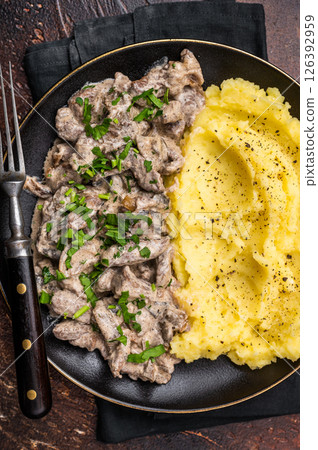 Beef stroganoff with mashed potatoes, fresh greenery and savory mushroom sauce in a plate . brown background. top view Beef stroganoff with mashed potatoes, fresh greenery and savory mushroom sauce in a plate . brown background. top view 126392959