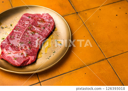 Marinated with olive oil and herbs Raw top sirloin or rump beef steak. orange background. top view 126393018