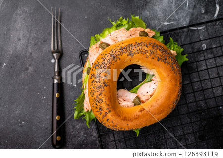Bagel sandwich with lox, smoked salmon, lettuce and cream cheese on a rack. black background. top view 126393119