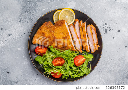 Fried Weiner schnitzel steak, veal breaded meat with salad on a plate. grey background. top view Fried Weiner schnitzel steak, veal breaded meat with salad on a plate. grey background. top view 126393172