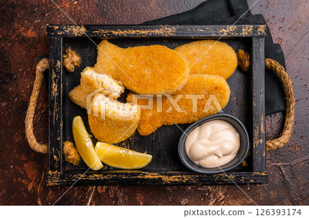 Crusted Fish sticks fingers with lemon and tartar sauce in wooden tray. brown background. top view Crusted Fish sticks fingers with lemon and tartar sauce in wooden tray. brown background. top view 126393174