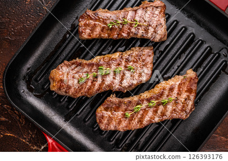 Grilled Tri tip steaks, marbled beef meat on pan with herbs. brown background. top view 126393176