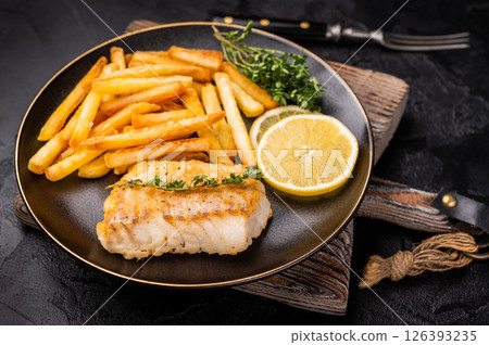 Homemade Fish and chips with roast cod whitefish fillet and fried potatoes on plate. black background. top view 126393235