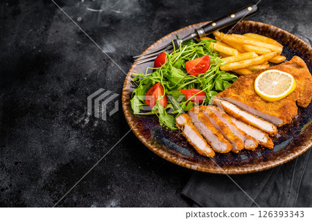 Roast viennese schnitzel steak, breaded meat with salad and french fry on a plate. black background. top view Roast viennese schnitzel steak, breaded meat with salad and french fry on a plate. black background. top view 126393343
