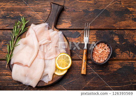 Freshly caught raw squid with glistening skin, perfect for grilling or frying to create mouthwatering dishes. wooden background. top view Freshly caught raw squid with glistening skin, perfect for grilling or frying to create mouthwatering dishes. wooden background. top view 126393569