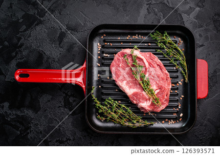 Raw Rib eye steak in a grill skillet with herbs, prime beef meat. black background. top view 126393571
