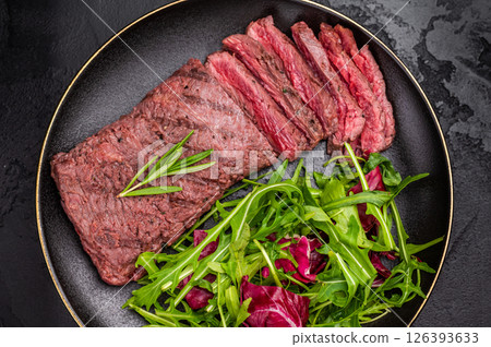 Grilled and sliced Flank beef steak on plate with salad. black background. top view 126393633