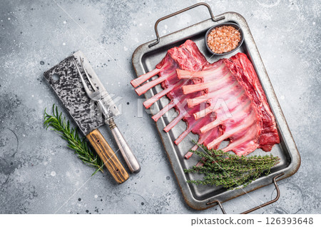 Raw mutton meat for chops steaks, uncooked rack of lamb on steel tray with herbs. grey background. top view Raw mutton meat for chops steaks, uncooked rack of lamb on steel tray with herbs. grey background. top view 126393648