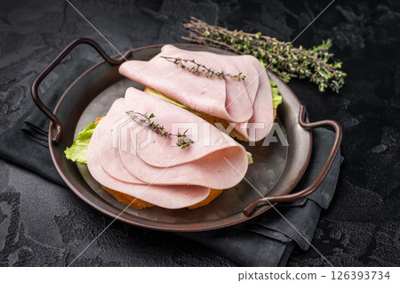 Delicious ham sandwich stacked high with fresh veggies, perfect for a quick lunch or picnic delight. black background. top view 126393734
