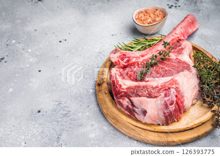 Uncooked tomahawk steak, raw black angus beef rib eye with bone on wooden board. grey background. top view Uncooked tomahawk steak, raw black angus beef rib eye with bone on wooden board. grey background. top view 126393775