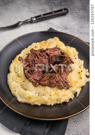 German Braised Beef Cheek, Slow cooked meat with smashed potatoes on a plate. grey background. top view German Braised Beef Cheek, Slow cooked meat with smashed potatoes on a plate. grey background. top view 126393787