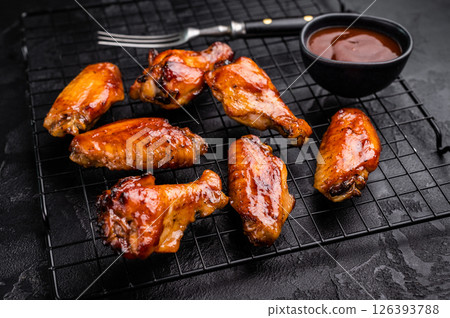Mouthwatering BBQ chicken wings, coated in a rich sauce, perfect for finger-licking appetizers at any gathering. black background. top view Mouthwatering BBQ chicken wings, coated in a rich sauce, perfect for finger-licking appetizers at any gathering. black background. top view 126393788
