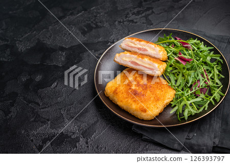Chicken cordon bleu cutlet with cheese and ham on plate with salad. black background. top view Chicken cordon bleu cutlet with cheese and ham on plate with salad. black background. top view 126393797