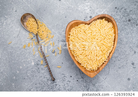 Raw Orzo pasta, uncooked dry Italian risoni in a bowl. grey background. top view Raw Orzo pasta, uncooked dry Italian risoni in a bowl. grey background. top view 126393924