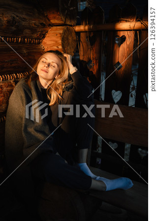 Woman enjoying peaceful moment in rustic cabin, wrapped in blanket. Warm lighting creates serene and tranquil atmosphere, perfect for relaxation and contemplation. Thoughtful woman sitting near window 126394157