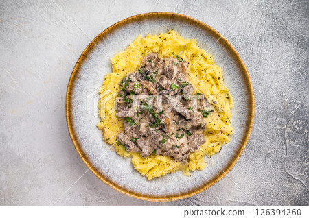 Plate of tender beef stroganoff served with creamy mashed potatoes and steaming gravy. grey background. top view 126394260
