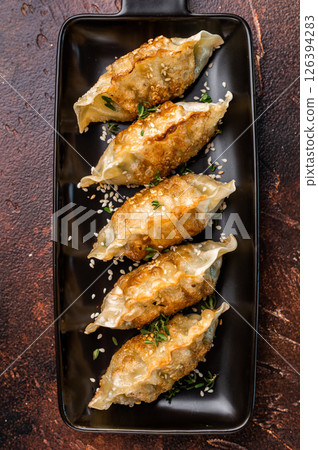 Fried Jiaozi on plate with sauce, Chinese Dumplings with shrimps and vegetables. brown background. top view Fried Jiaozi on plate with sauce, Chinese Dumplings with shrimps and vegetables. brown background. top view 126394283