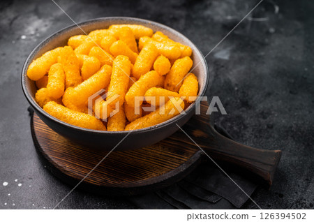 Deliciously addictive cheese flavored corn puffs, beautifully arranged on a plate. black background. top view Deliciously addictive cheese flavored corn puffs, beautifully arranged on a plate. black background. top view 126394502