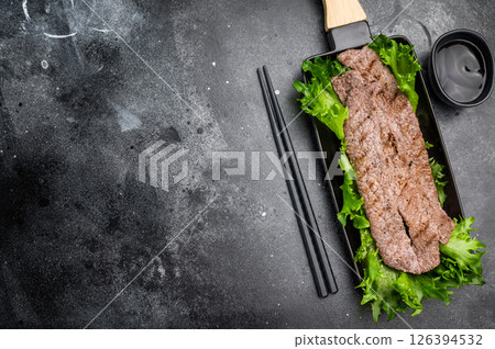 Sizzling yakiniku wagyu bees strips, featuring an array of marinated meats and fresh vegetables, grilled to perfection. A delightful Japanese BBQ. black background. top view 126394532