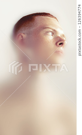 Creative portrait. Young man with red buzzcut looks into distance through hazy frame with warm light. Introspective mood evokes thought, curiosity. Creative portrait. Young man with red buzzcut looks into distance through hazy frame with warm light. Introspective mood evokes thought, curiosity. 126394774