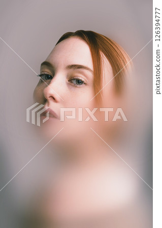 Surreal collage. Red-haired woman looks sideways with piercing eyes through translucent veil effect. Cold color tones suggest distance and reflection Surreal collage. Red-haired woman looks sideways with piercing eyes through translucent veil effect. Cold color tones suggest distance and reflection 126394777