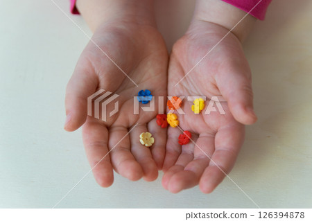 Hands of the child holding the little toys on the wood background. Colorful plastic flowers in the child hands.  126394878