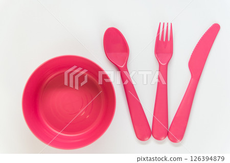 Plastic pink spoon, knife, fork located near pink plate on the white background. Flat lay. Top view.  126394879