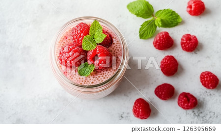 A jar of creamy chia pudding topped with fresh raspberries and mint leaves, placed on a clean white table with soft natural light, concept of healthy eating 126395669