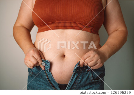 Woman struggling to fit in tight jeans, weight and body image concept 126396259