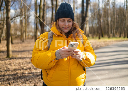 Smiling Woman in Yellow Jacket Walking in the Park Holding a Phone 126396263