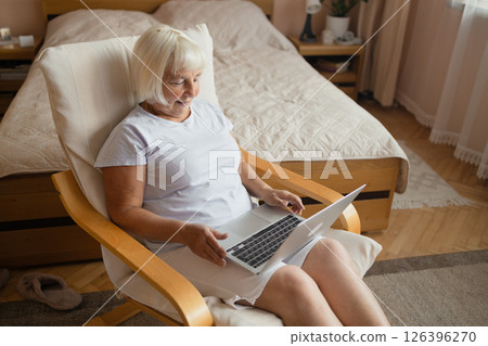 Senior Woman Using Laptop While Sitting Comfortably at Home in Cozy Bedroom Interior Senior Woman Using Laptop While Sitting Comfortably at Home in Cozy Bedroom Interior 126396270
