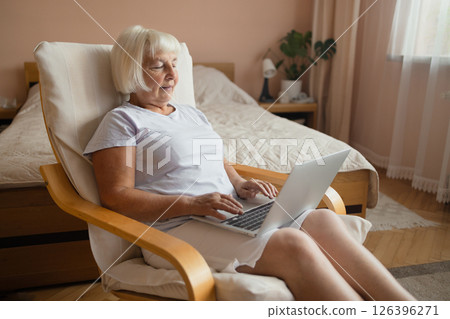 Senior Woman Using Laptop While Sitting Comfortably at Home in Cozy Bedroom Interior Senior Woman Using Laptop While Sitting Comfortably at Home in Cozy Bedroom Interior 126396271