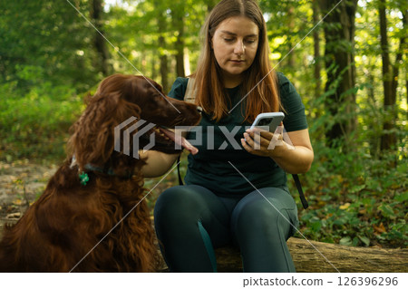 Woman Using Smartphone While Sitting with Dog in the Forest 126396296