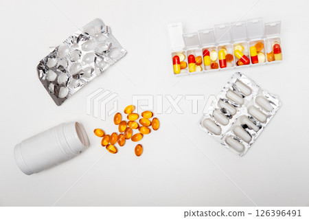 pillbox by days of the week with fish oil and various pills, capsules and jars scattered on a white background, top view pillbox by days of the week with fish oil and various pills, capsules and jars scattered on a white background, top view 126396491