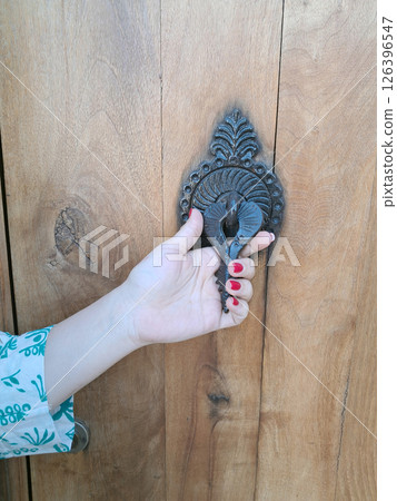 Woman hand holding a vintage doorknob on wooden door Woman hand holding a vintage doorknob on wooden door 126396547