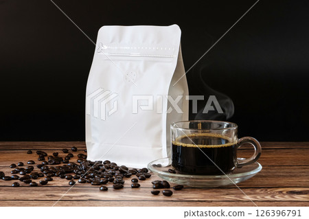 Roasted coffee beans in white paper bag with zipper on wooden table, blank mockup coffee bag template for product design advertising, black coffee hot stream in coffee cup on set 126396791