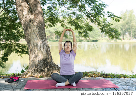 Wellness and Mindfulness. A woman practicing yoga and stretching outdoors by a serene lake. 126397037