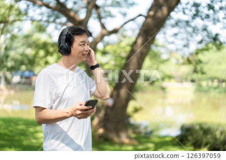 Wellness and Relaxation. Senior man enjoying music outdoors in a park with headphones. Wellness and Relaxation. Senior man enjoying music outdoors in a park with headphones. 126397059
