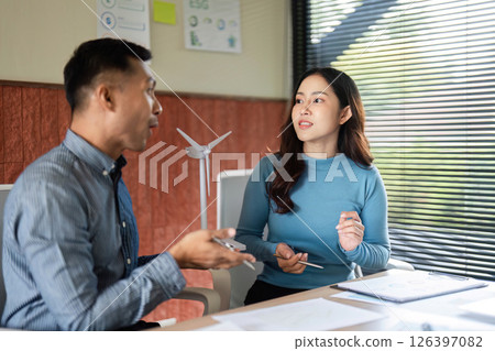 ESG Strategy Session. Professionals discussing environmental initiatives with a wind turbine model. ESG Strategy Session. Professionals discussing environmental initiatives with a wind turbine model. 126397082