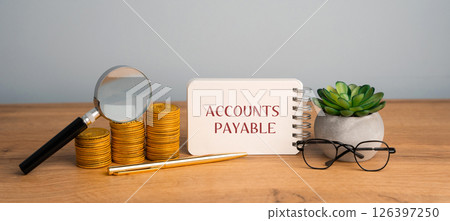 Accounts payable concept. Amount of money a company owes to its suppliers or creditors for goods and services received but not yet paid for. Notebook with inscription, stacks of coin, magnifying glass 126397250