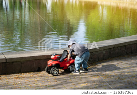 Four year old toddler boy playing with toy motorcycle near lake on sunny day. Outdoor activities, fun and games Four year old toddler boy playing with toy motorcycle near lake on sunny day. Outdoor activities, fun and games 126397362
