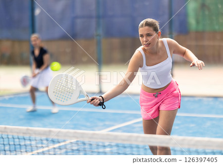 Woman standing behind net on tennis court 126397405