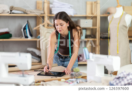 Tailor drawing fashion design on tablet in workshop 126397600