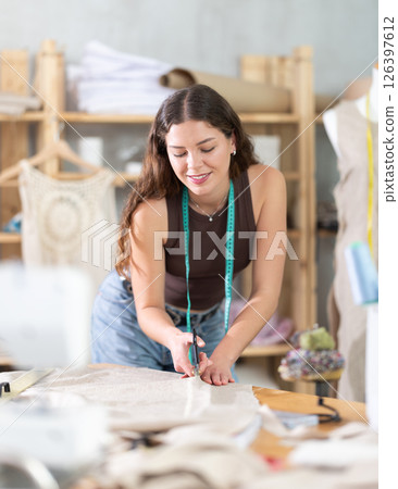 Young female dressmaker cutting textile in sewing workshop 126397612