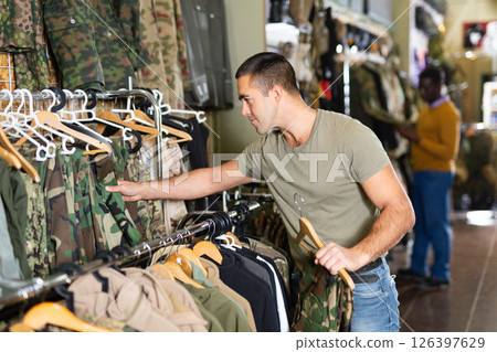 Guy choosing camouflage uniform in military shop Guy choosing camouflage uniform in military shop 126397629